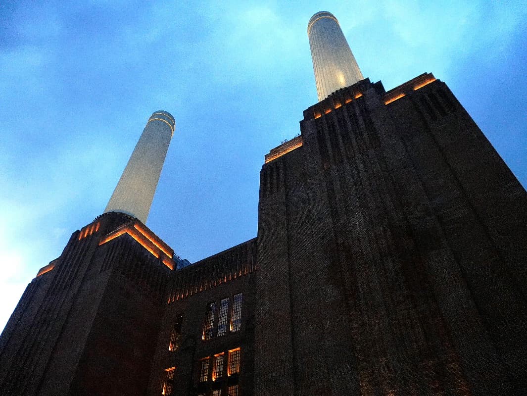 Battersea Power Station's brick towers and white chimneys uplit against a deep blue dusk sky