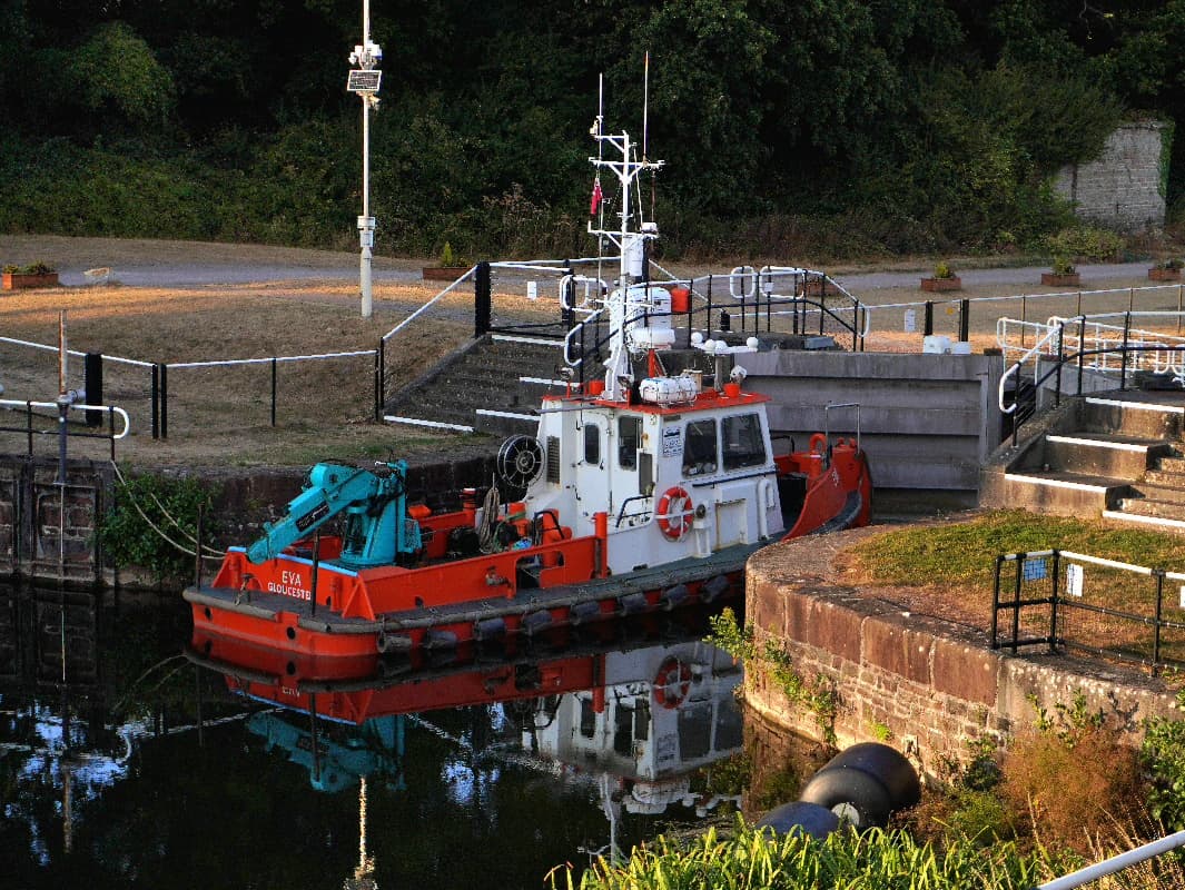 The red and white workboat Eva of Gloucester moored beside a canal lock in low evening sun