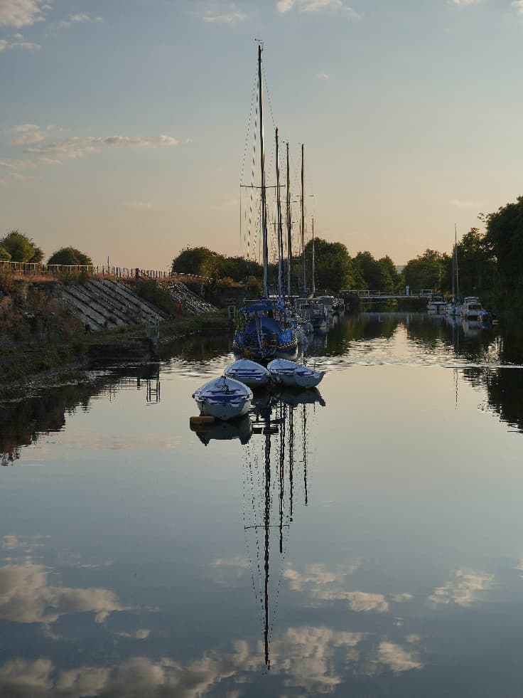 Yachts and small boats moored on still water at dusk, their masts mirrored in the surface